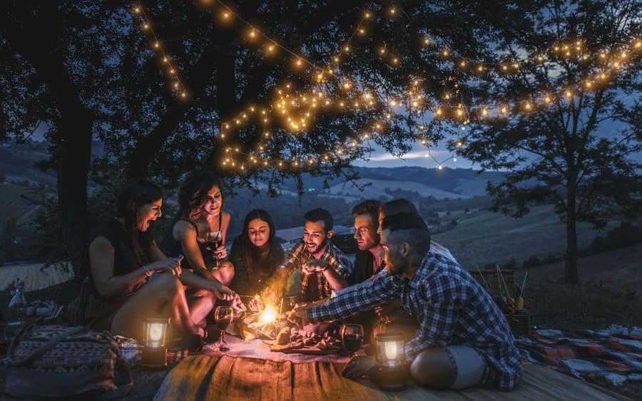 People sitting in a campsite with a string of lights over their heads