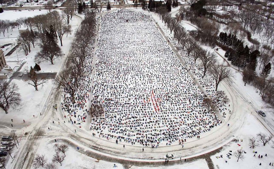 Aerial view of the hundreds of people out in the field all doing snow angles together. 