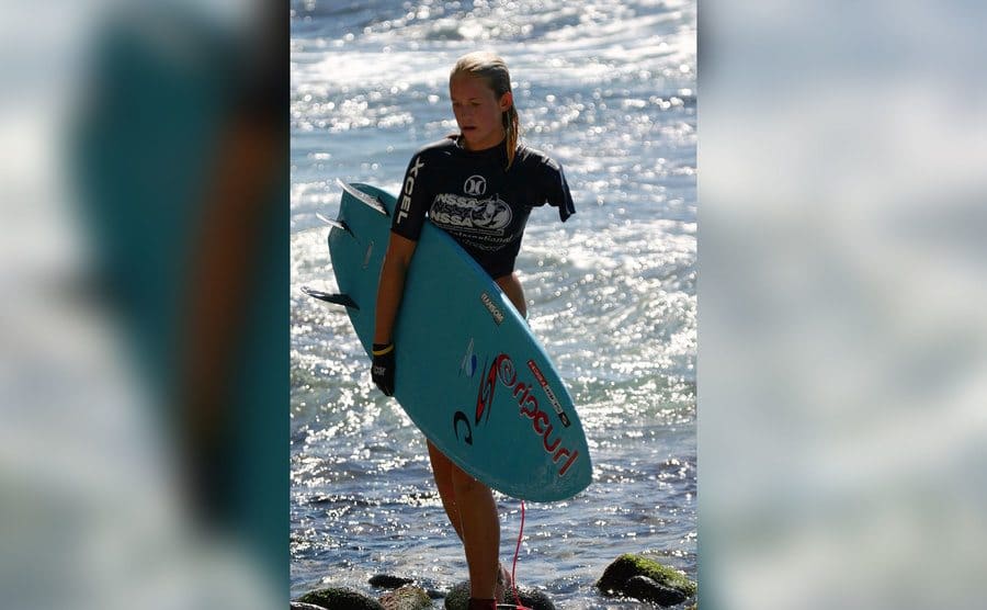 A young Bethany Hamilton coming out of the water surfboard in hand. 