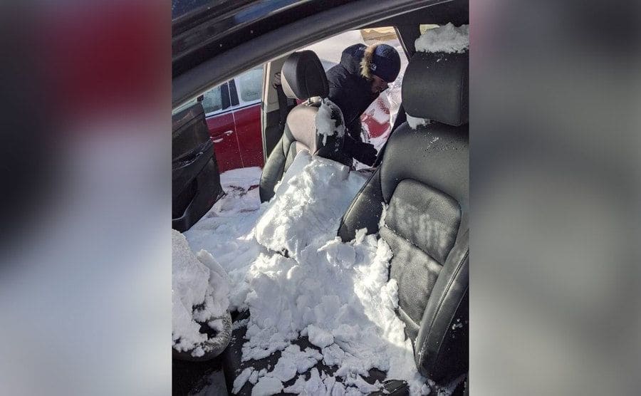 A man is trying to get out some of the snow that has gotten all over the inside of his car. 