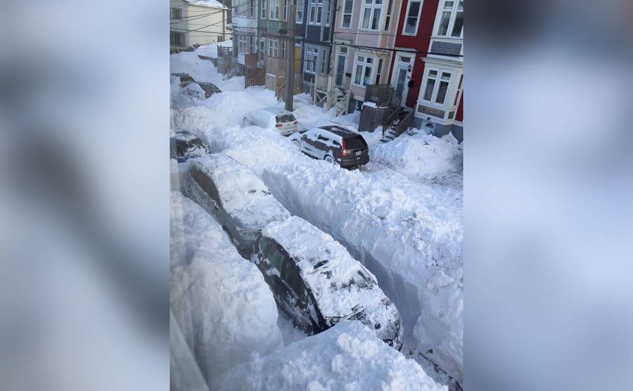Cars parked on the street with a wall of snow dividing between them. 