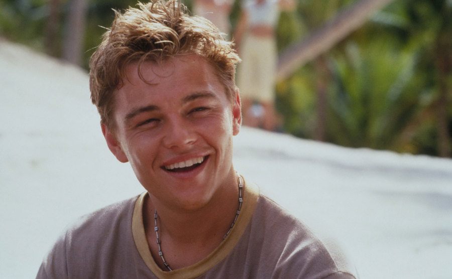 Leonardo DiCaprio sits by the beach in a movie still. 
